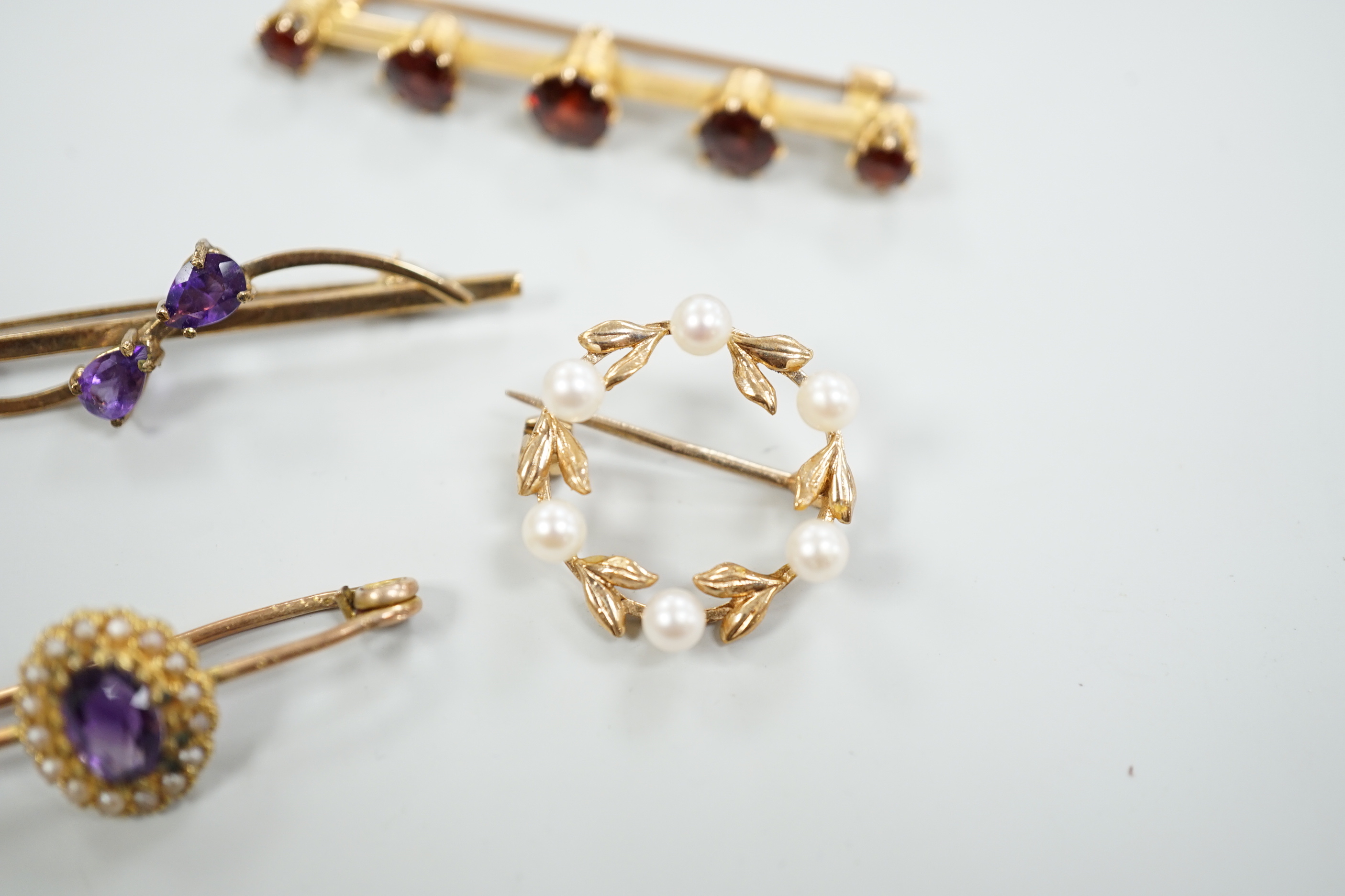 A 15ct and graduated five stone garnet set bar brooch, 48mm, a similar amethyst and seed pearl cluster set brooch and two other gem set brooches, including 9ct gold.